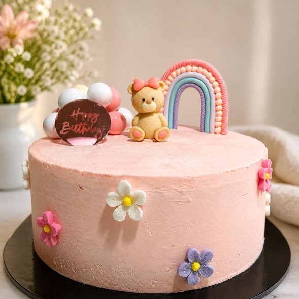 Pink birthday cake with a fondant bear, rainbow, flowers, and balloons